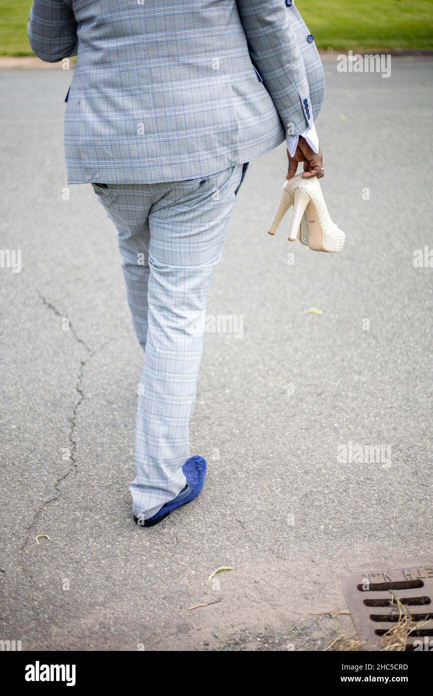 Vertikale Aufnahme eines Bräutigams, der auf der Autobahn läuft und in der Hand weiße Schuhe der Braut hält Stockfoto