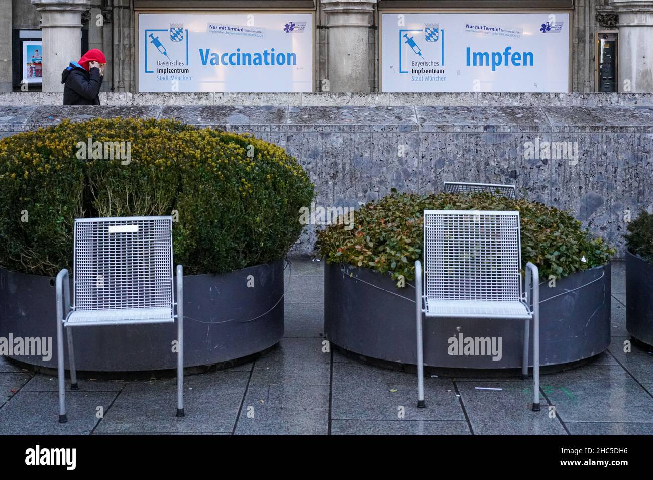 Zwei Stühle stehen auf einem Platz vor zwei übergroßen Pflanzgefäßen. Ansicht eines Werbebanners eines Impfzentrums. Stockfoto