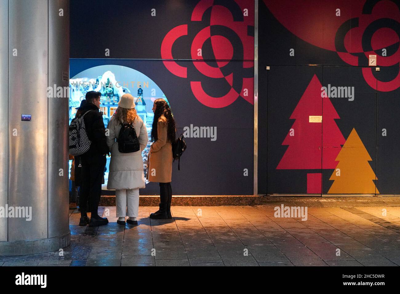 Schaufenster vor einem für Weihnachten geschmückten Kaufhaus. Ein junger Mann und zwei junge Frauen sprechen vor dem Display. Stockfoto