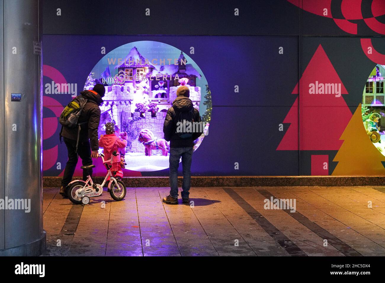 Schaufenster vor einem für Weihnachten geschmückten Kaufhaus. Ein Vater mit einem Kind und ein Mann schauen sich die Displays an. Stockfoto