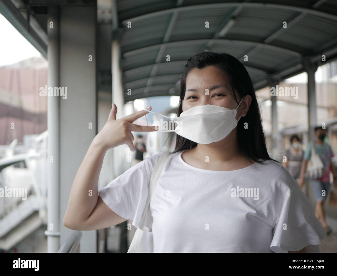 Eine südostasiatische Frau, die eine medizinische Maske vor ihrem Gesicht in der Überquerung hält Stockfoto