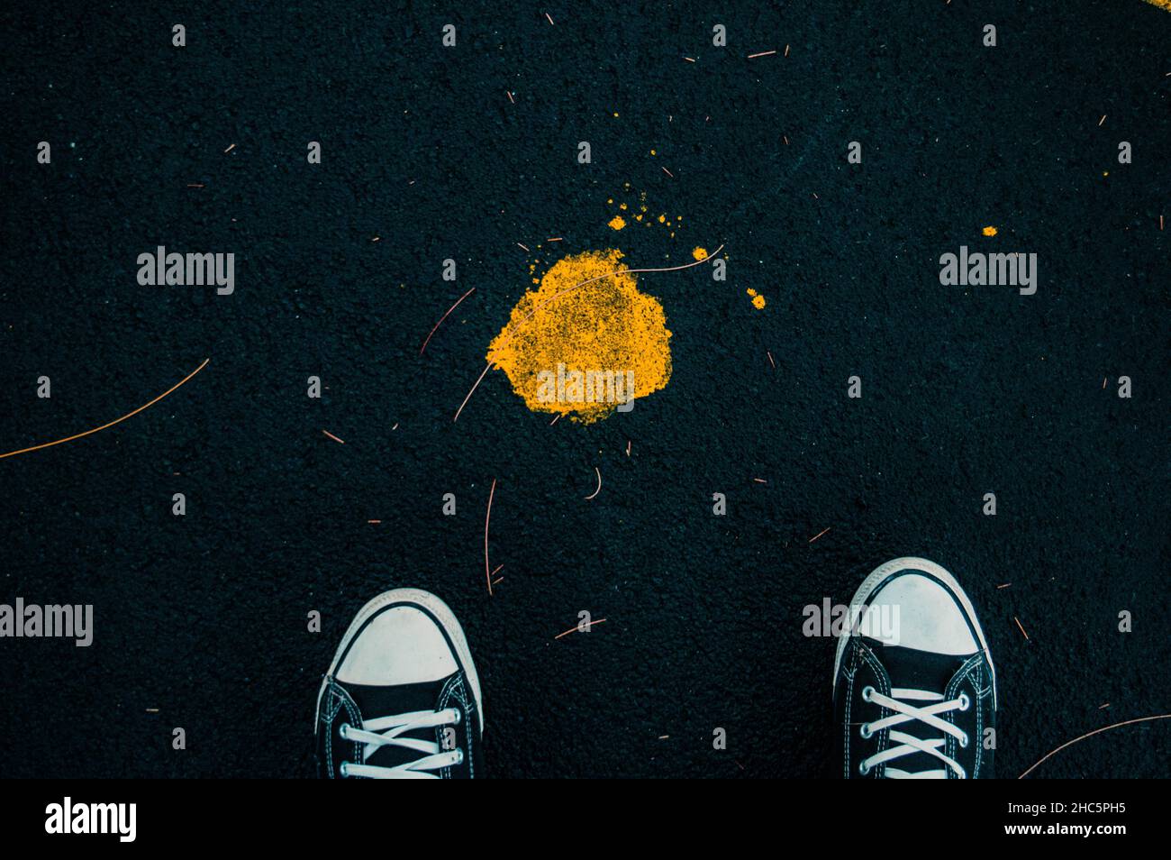 Ein großer Winkel von einigen Füßen und ein gelber Farbfleck auf dem Asphalt Stockfoto