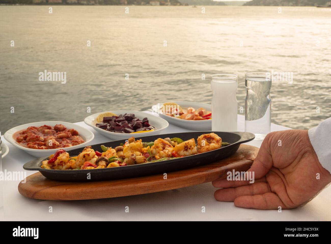 Der Kellner hat das Essen am Meer auf den Tisch gelegt. Türkische Vorspeisen Stockfoto