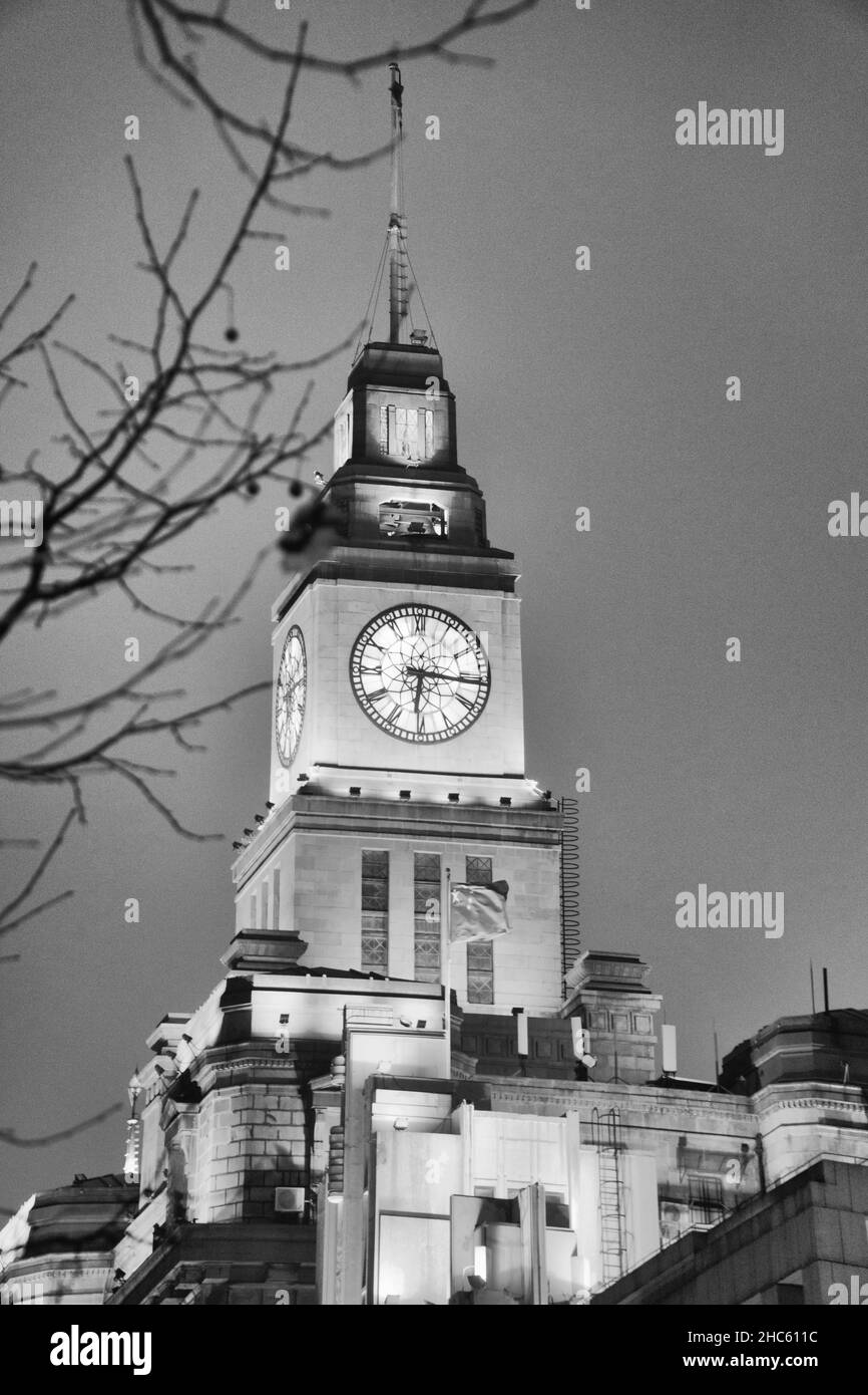 Schwarz-Weiß-Vintage-Foto von trockenen Ästen und der alten Big Clock auf einem hohen Turm im Shanghai Custom House, China im Winter Stockfoto