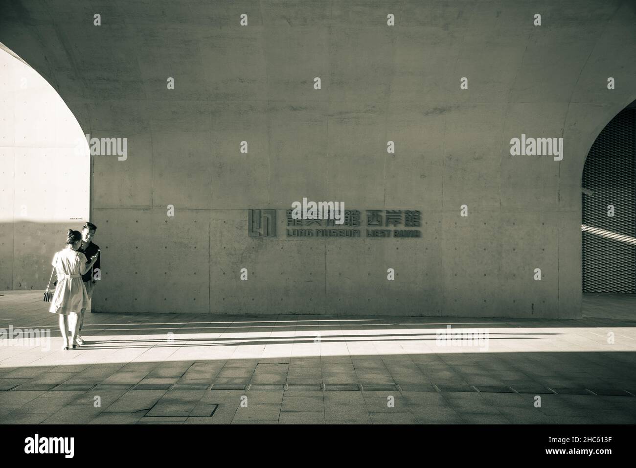 Ein Schwarz-Weiß-Foto eines Paares, das gemütlich vor dem Hintergrund englischer und chinesischer Schriften des West Bund Long Museums in Shanghai, China, steht Stockfoto