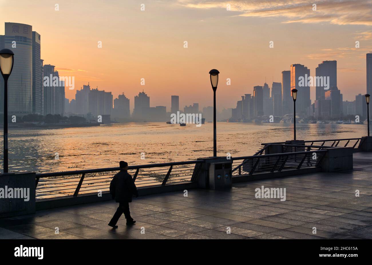 Ein Mann geht am Morgen allein vor dem Hintergrund des Huangpu-Flusses und des orangen Himmels am Ufer des Huangpu-Flusses, des Bundes, Shanghai Stockfoto