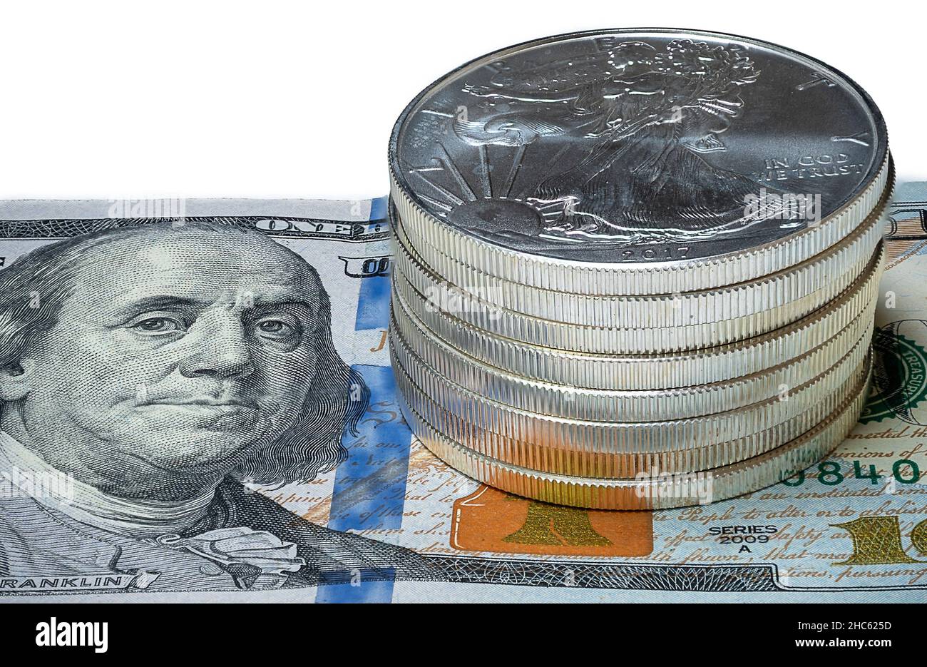 Nahaufnahme eines Stapels Silberadler-Münzen (Bullions) auf einem US-Bill aus dem Jahr $100 auf isoliertem weißem Hintergrund Stockfoto