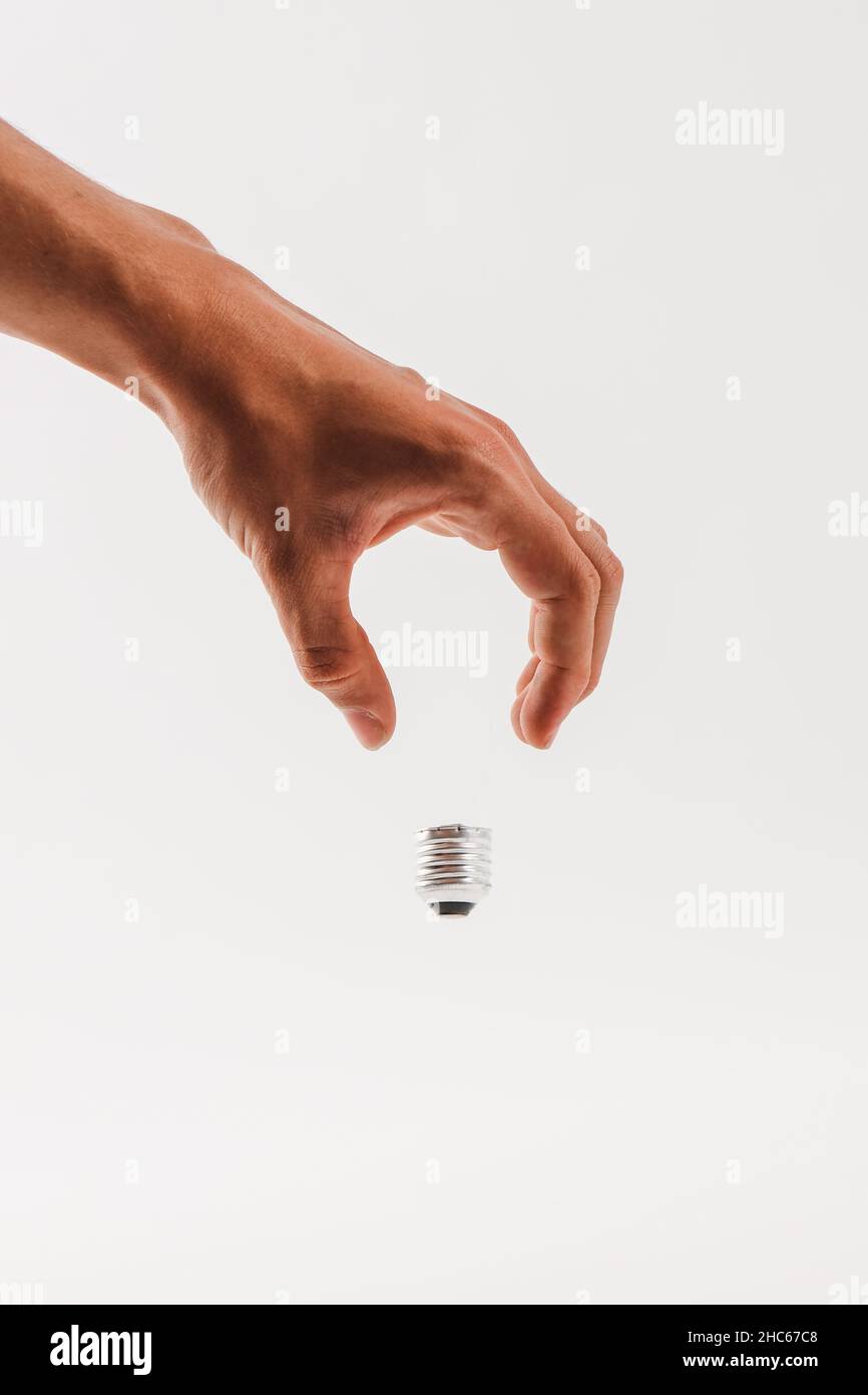 Vertikale Aufnahme einer menschlichen Hand, die eine halb unsichtbare Glühbirne auf weißem Hintergrund hält Stockfoto