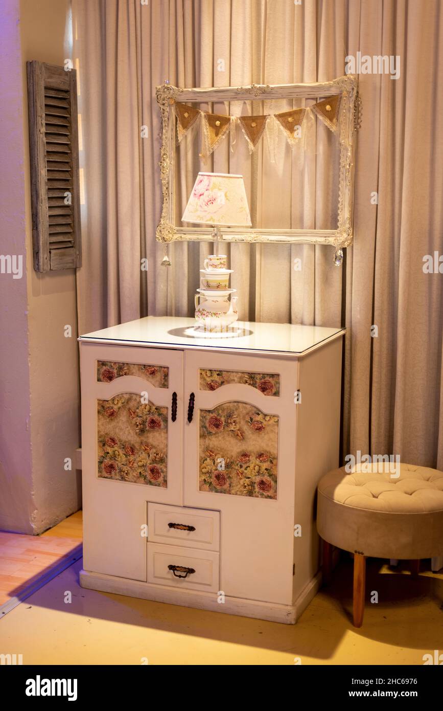 Schöner beigefarbener Tisch mit Vintage-Lampe, Rahmen, kleinem Stuhl und Vorhang, moderne Innenräume Stockfoto