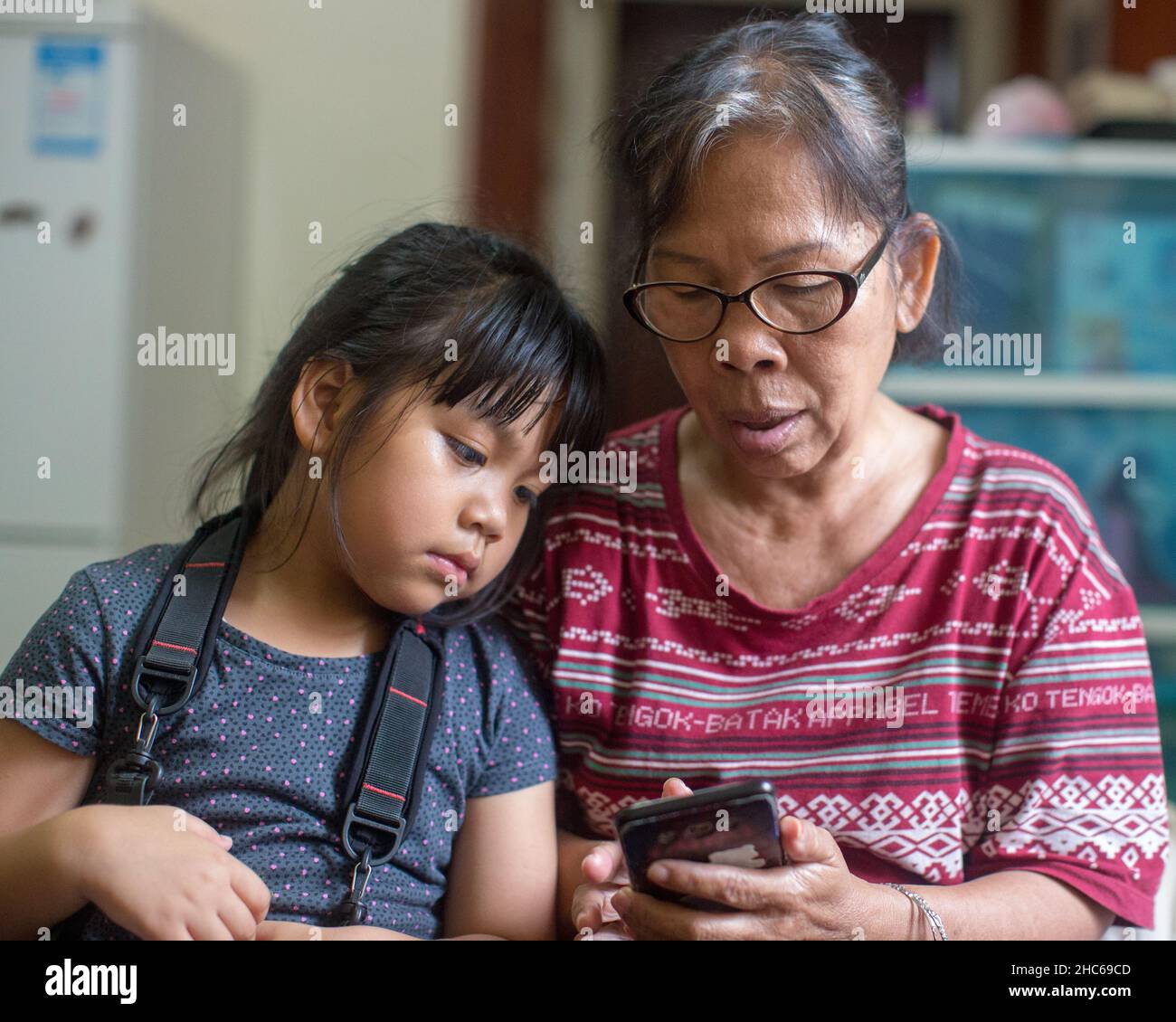 Ein Mädchen mit einem Kameragurt und ihre Großmutter betrachten zusammen ein Foto auf einem Handy in einer Wohnung in Shanghai, China, Asien Stockfoto