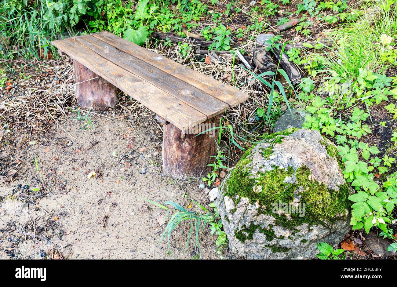 Handgemachte Holzbank und moosiger Stein am Ufer des Sees im Sommer Stockfoto