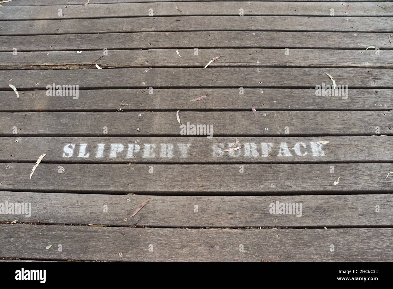 Ein Holzweg mit einem Warntext „lipprige Oberfläche“ Stockfoto