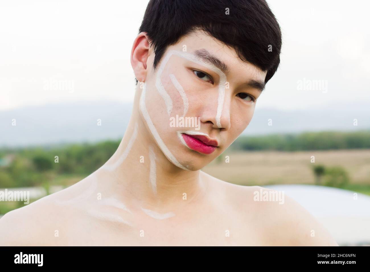 Ein schwul-hübscher Mann aus Asien, der kein Hemd trägt, schreibt auf das Gesicht und trägt einen pinken Lippenstift. Speicherplatz kopieren Stockfoto