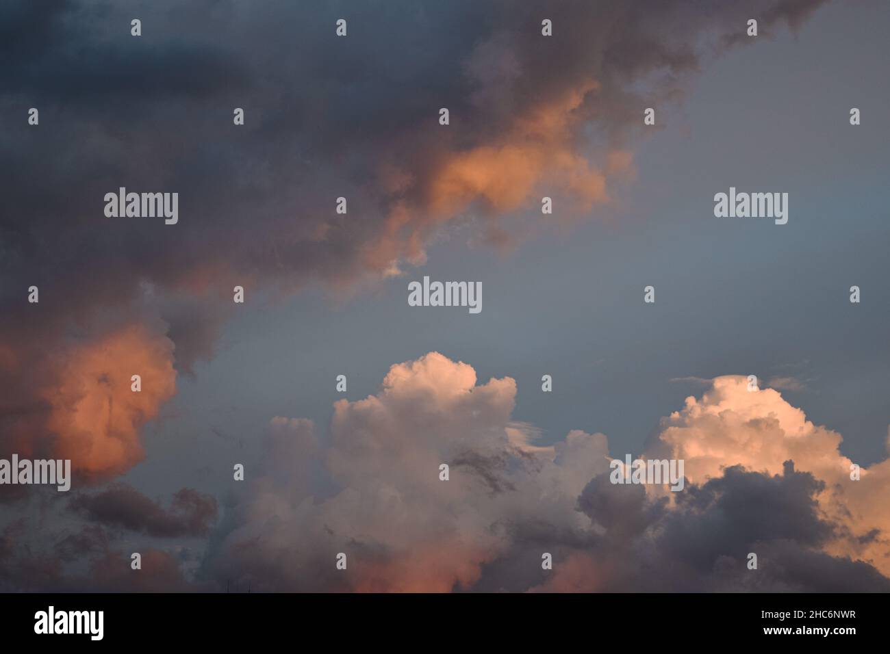 Blick auf große wogende Wolken im Hintergrund, die zum Teil durch lange, schattige Wolken bei Sonnenuntergang verborgen sind Stockfoto