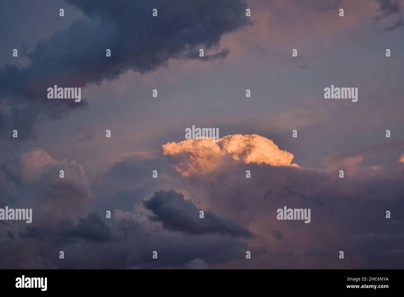Blick auf große wogende Wolke im Hintergrund, teilweise versteckt durch lange, schattige Wolken bei Sonnenuntergang Stockfoto