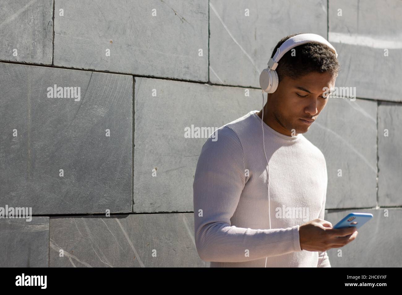 Der Mann genießt es, Musik über Kopfhörer mit seinem Telefon zu hören, horizontale Ansicht mit Sonnenlicht Stockfoto