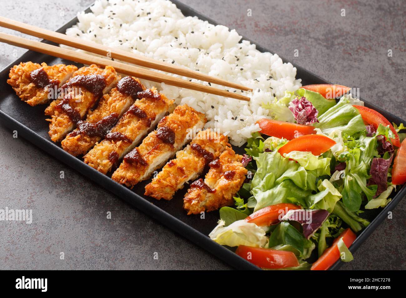 Chicken Katsu ist ein japanisches Gericht, das auch als Panko-Huhn oder Tori Katsu bekannt ist und mit Reis- und Gemüsesalat auf dem Betontisch serviert wird. Horizont Stockfoto