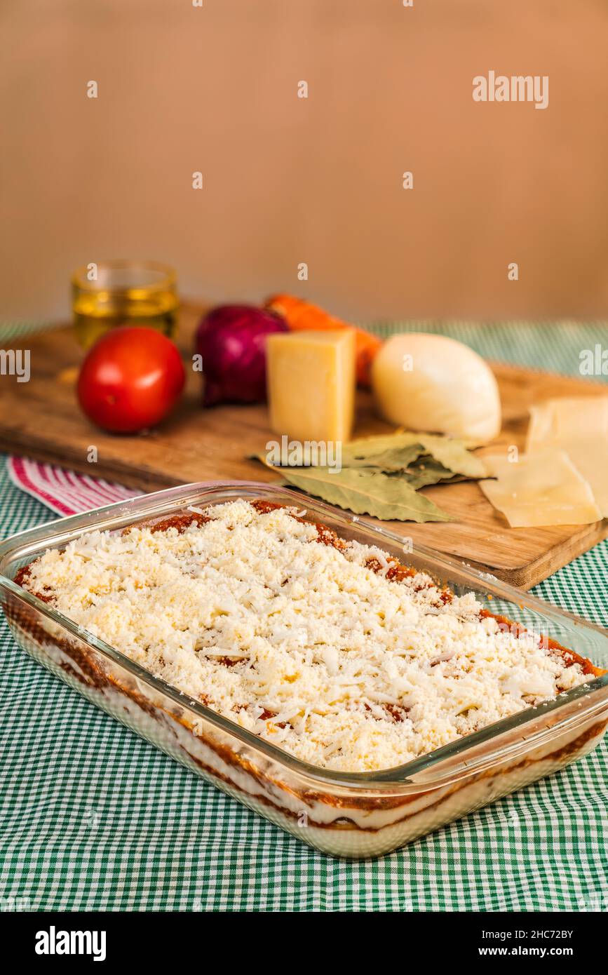 Vertikales Bild von hausgemachter Lasagne in einem Glastablett, bereit zum Kochen mit Zutaten dahinter Stockfoto