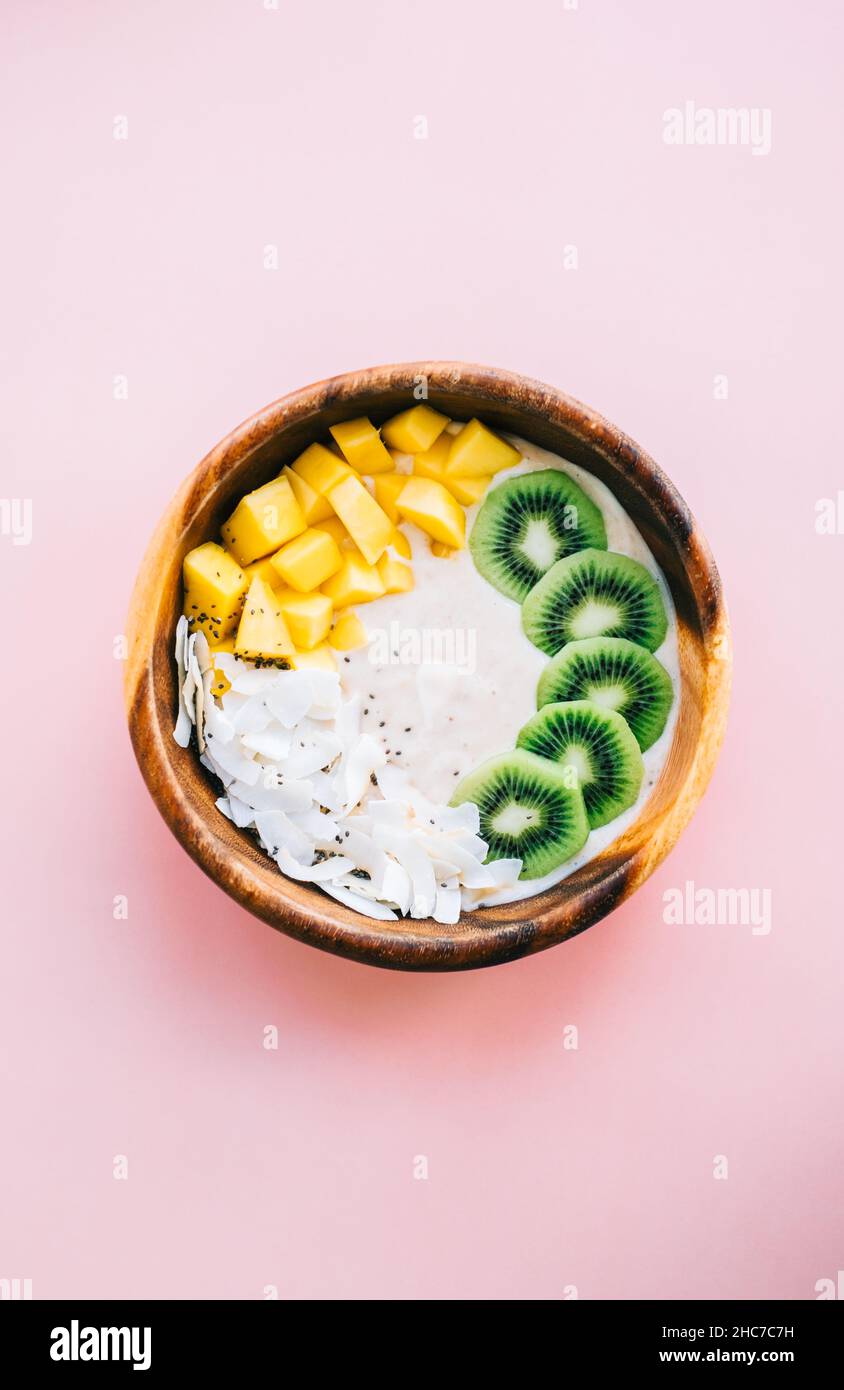 Gesunde Frucht-Smoothie-Schale mit Mango, Kokosnusschips und Kiwi auf rosa Hintergrund. Stockfoto