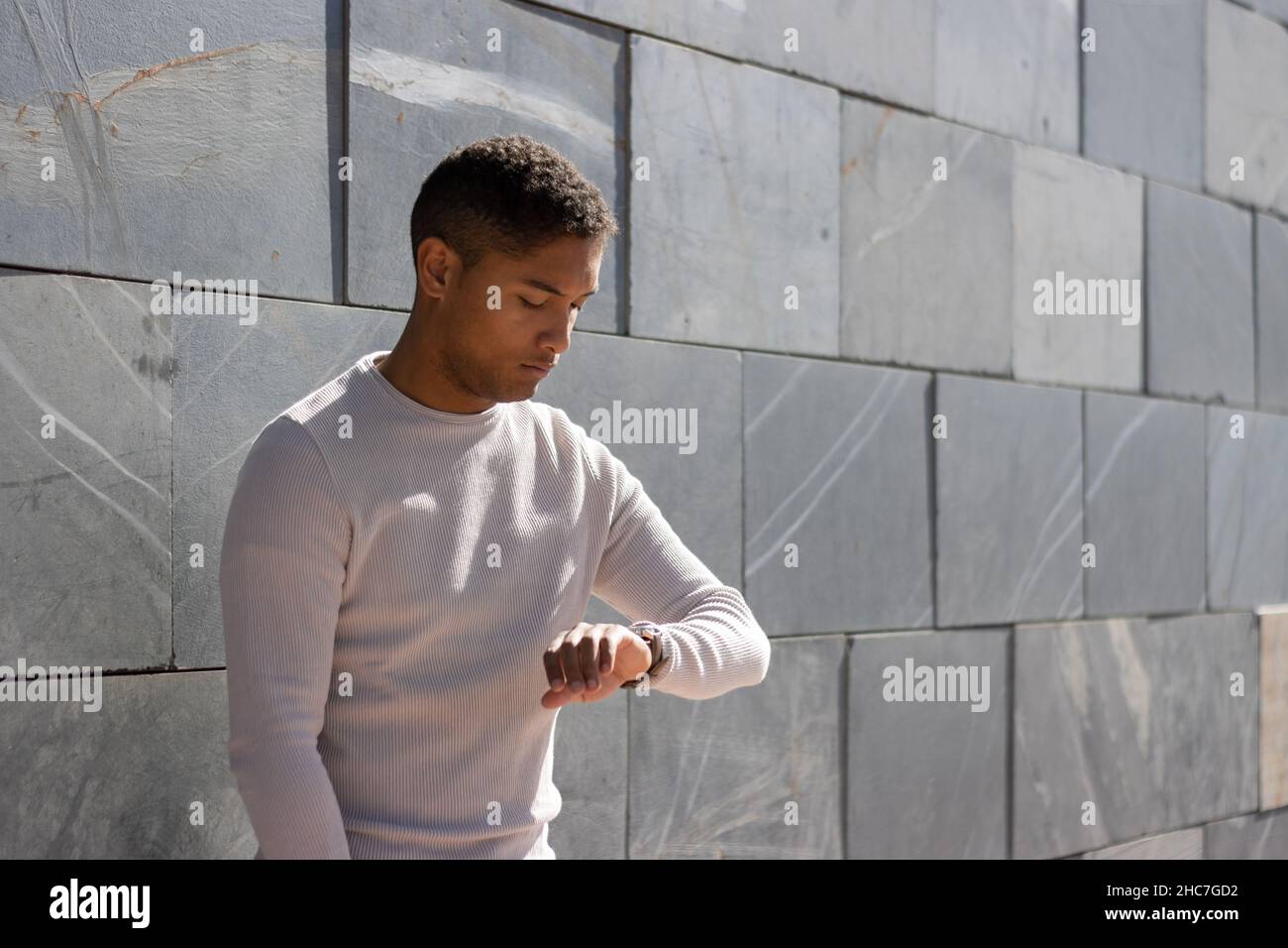 Junger schwarzer Latino-Junge, der auf die Uhr an einer grauen Wand auf der Straße schaut Stockfoto