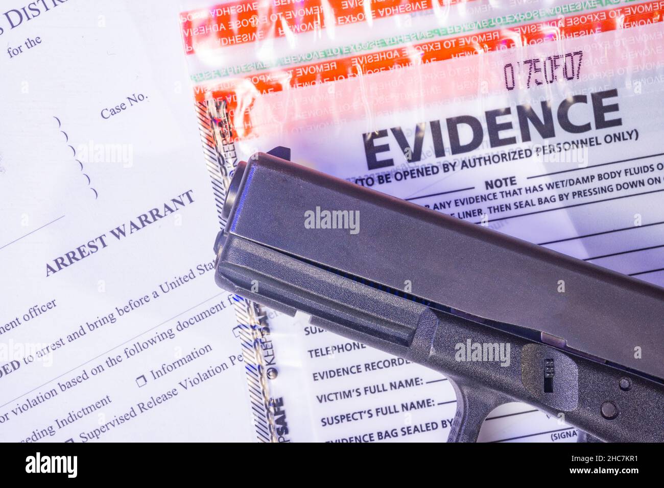 Eine Schusswaffe sitzt auf einem Beweisbeutel und einem Haftbefehl. Stockfoto