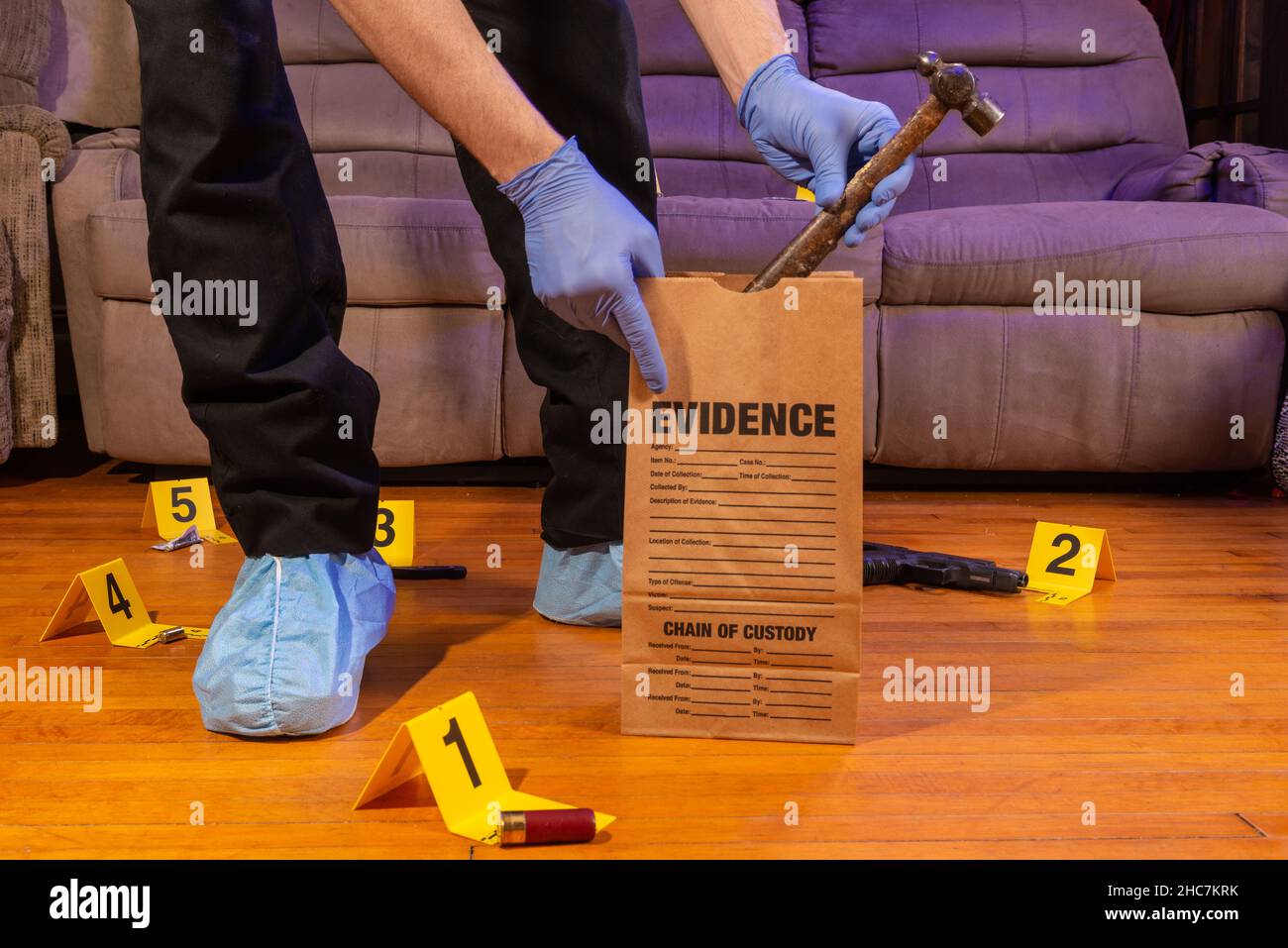 Ein Techniker am Tatort legt einen Hammer in einen Beweisbeutel mit anderen Beweisstücken, die an einem Tatort verstreut sind. Stockfoto