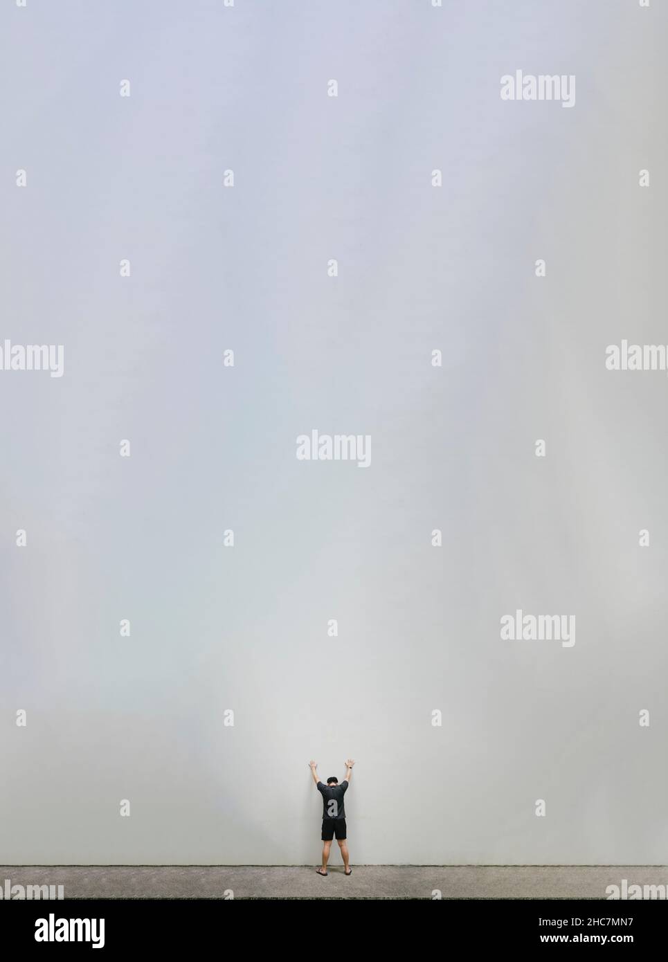 Winziger Mann, der vor einer riesigen, weißen Wand steht Stockfoto