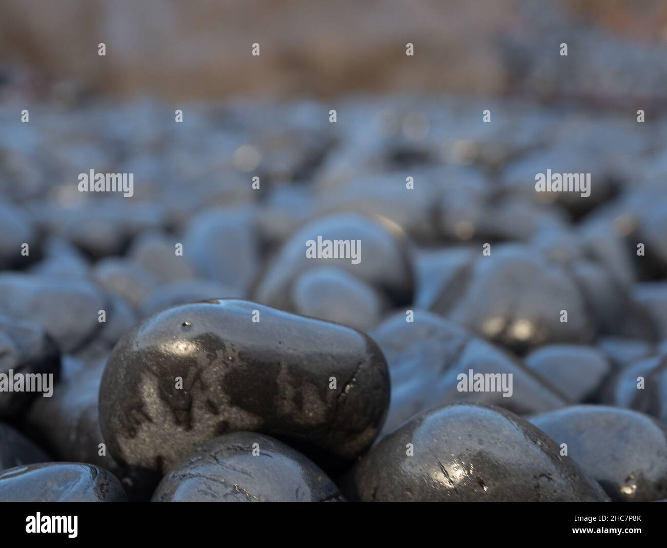 Nahaufnahme des glatten, nassen, schwarzen Vulkangesteins Cobble Beach bei Yaquina Head an der Küste von Oregon. Fotografiert mit geringer Schärfentiefe. Stockfoto