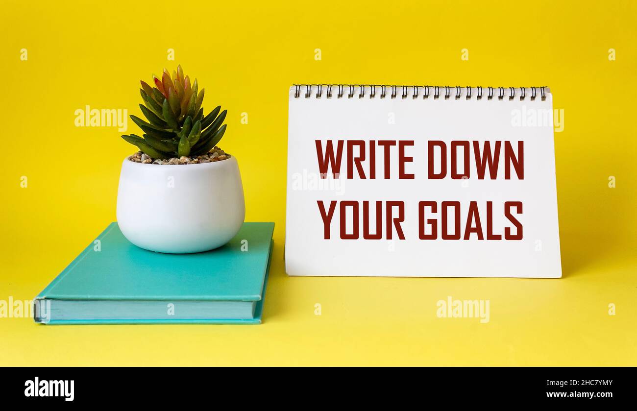 Phrase Schreiben Sie Ihre Ziele auf Notizblock und gelben Hintergrund mit grünem Tagebuch und Kaktusblüte geschrieben. Ziele und Pläne Stockfoto