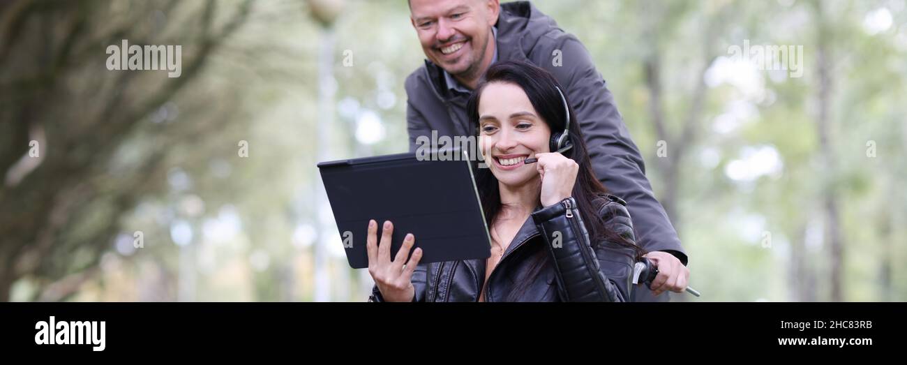 Frau im Rollstuhl und Mann, der im Park auf einem digitalen Tablet spricht Stockfoto