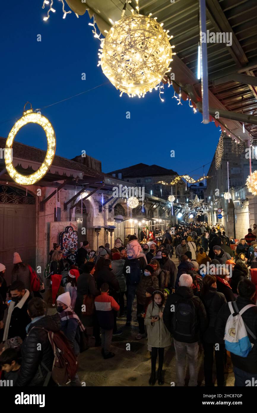 Jerusalem, Israel. 25th Dez 2021. Am 25. Dezember 2021 gehen die Menschen in Jerusalem, Israel, entlang einer weihnachtlich geschmückten Bab el Gadid Straße im christlichen Viertel der Altstadt. Israelis, die aufgrund der COVID-19-Omicron-Variante nicht ins Ausland reisen konnten, füllten die weihnachtlichen Gassen des Christlichen Viertels. Kredit: Eddie Gerald/Alamy Live Nachrichten Stockfoto