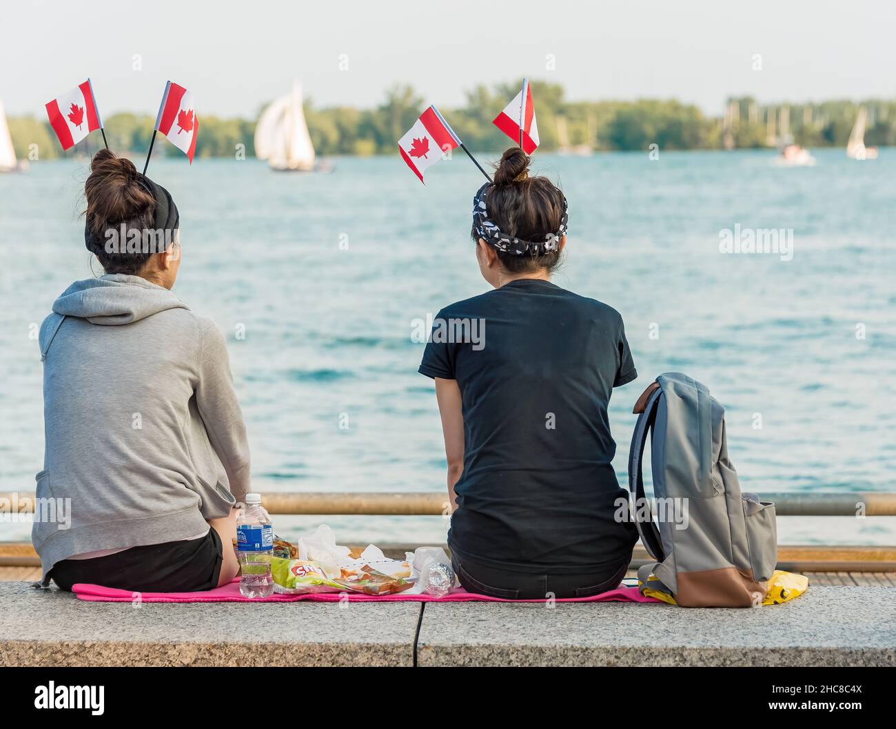 Toronto, Kanada - 1. Juli 2015: Kanadas Tag feiert, Freunde genießen einen Tag in der Toronto Harbourfront.zwei Mädchen sitzen und essen am Strand Stockfoto