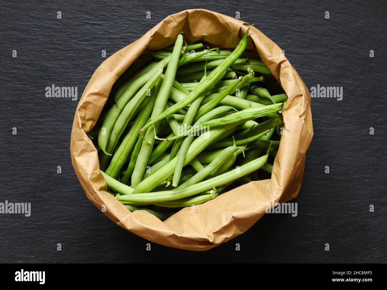 Fotografie von grünen Bohnen in einer braunen Papiertüte auf Schieferhintergrund für Lebensmittelillustrationen /die grüne Bohne, auch grüne Bohne genannt, ist eine Vielzahl von Gewehren Stockfoto