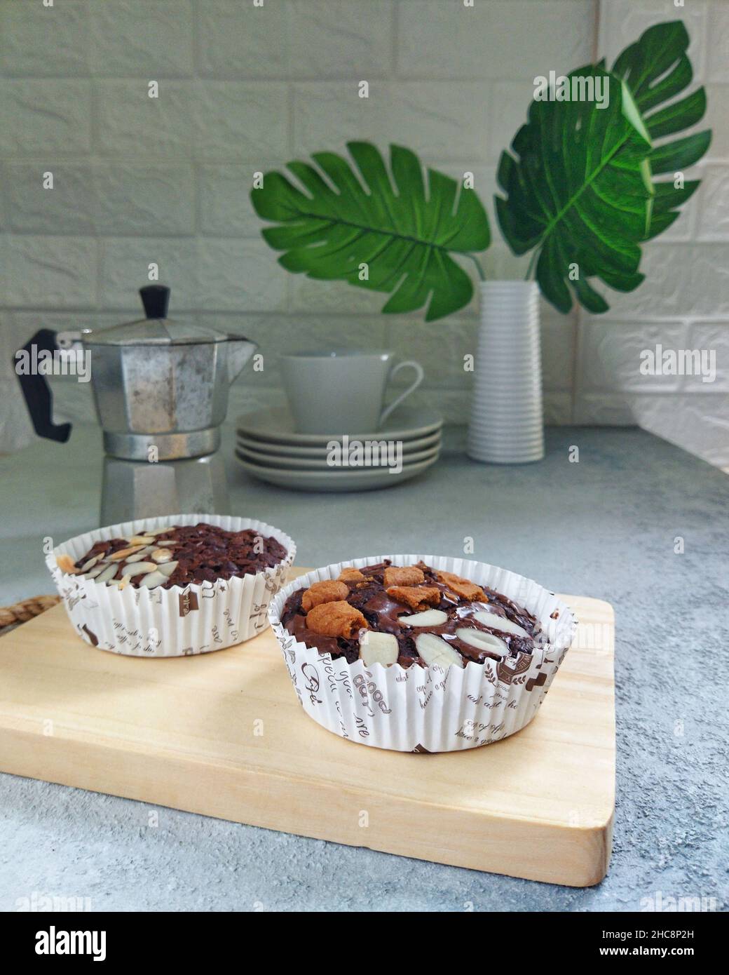 Brownies auf einem Schneidebrett, Mokapot, eine Tasse Kaffee und Pflanzen auf einem rustikalen Tisch Stockfoto