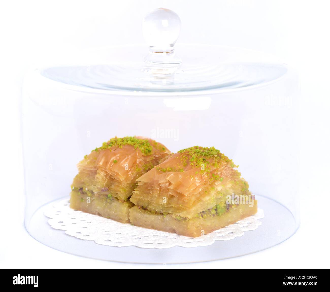 Frisches Baklava, ein orientalisches Gebäck aus Blätterteig und Nüssen, liegt unter einer Glashaube auf einem weißen Deckchen vor einem weißen Hintergrund Stockfoto