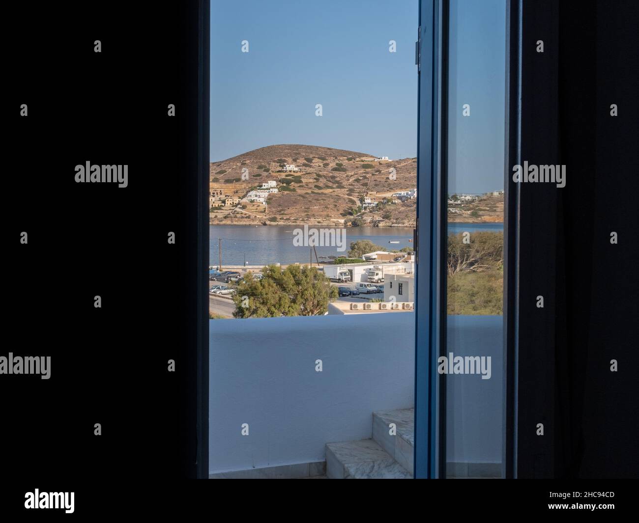 Blick auf das Meer durch ein Hotelzimmerfenster ohne Menschen. Aufgenommen an einem Morgen eines sonnigen Sommertages auf der ägäischen Insel iOS, Griechenland Stockfoto