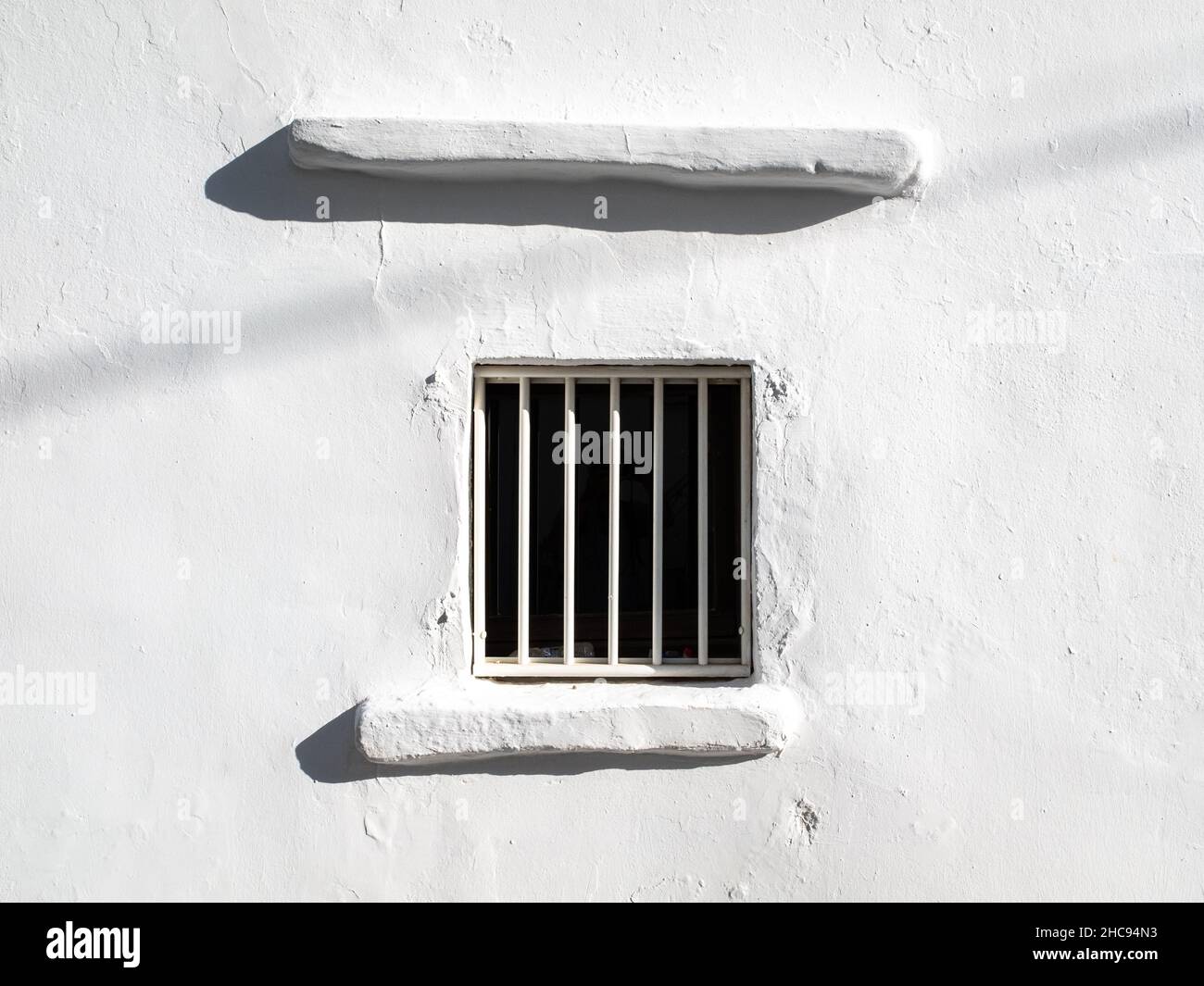 Typisches Fenster mit geschlossenen Bars an einem weißen Wandhaus. Aufgenommen an einem sehr sonnigen Sommertag auf der Ägäischen Insel Santorini, Griechenland Stockfoto