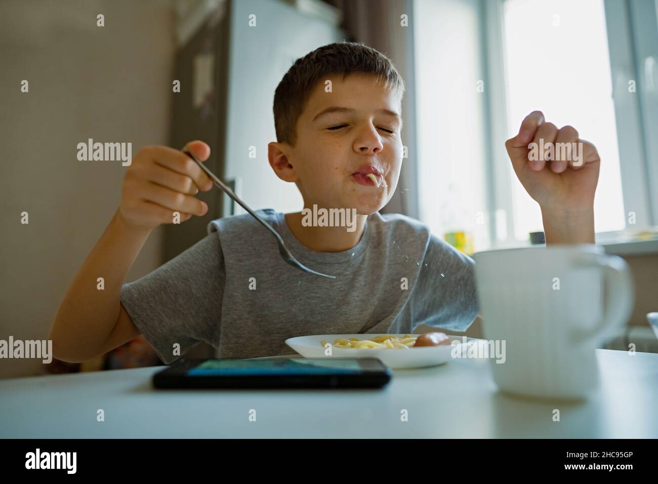 Fröhlicher, hungriger Junge isst Nudeln mit Appetit, saugt Nudeln spielerisch ein Stockfoto