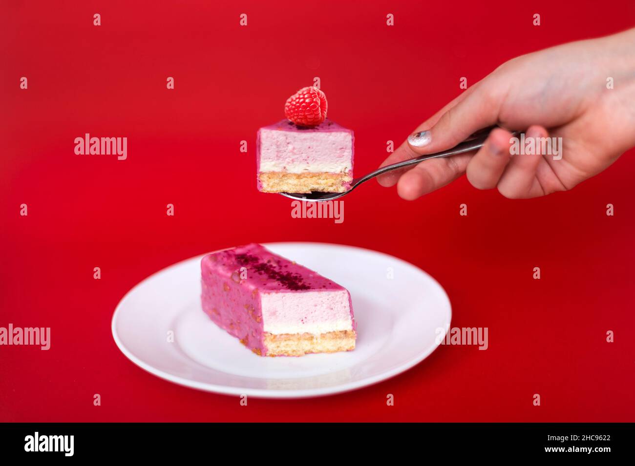Mousse-Kuchen in der Hand einer Frau mit Himbeeren auf rotem Hintergrund. Stockfoto