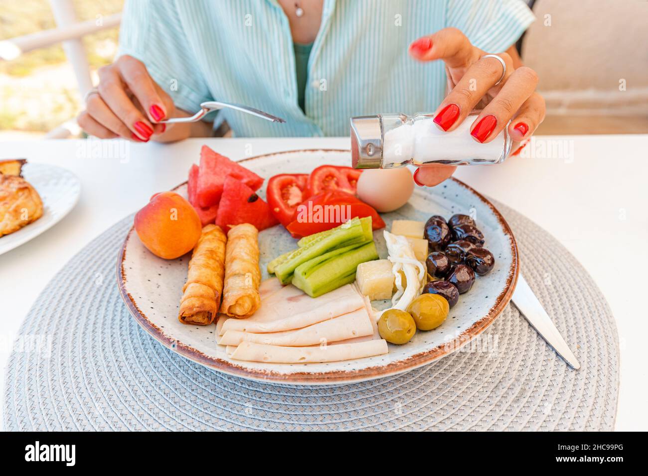 Glückliche Frau mit Salzkeller in der Hand Würze Gericht mit überschüssigem Salz oder Pfeffer in einem Restaurant. Ungesunde Essgewohnheiten führen zu Krankheiten Stockfoto