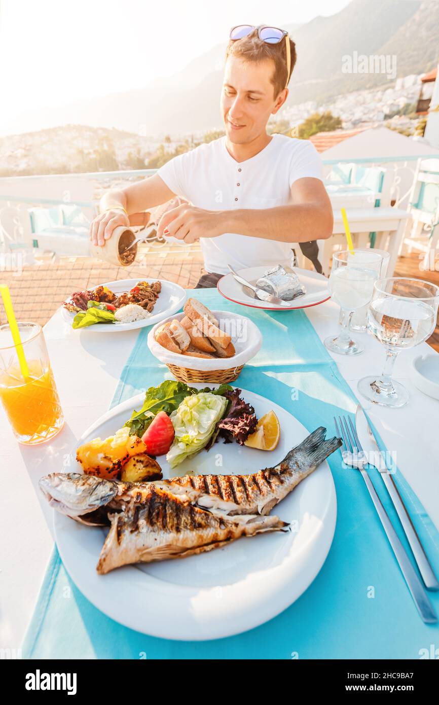 Fröhlicher Mann mit gegrilltem Seebassfisch und anderen Gerichten in einem Fischrestaurant. Das Konzept der mediterranen Ernährung und des epicure Lifestyles Stockfoto
