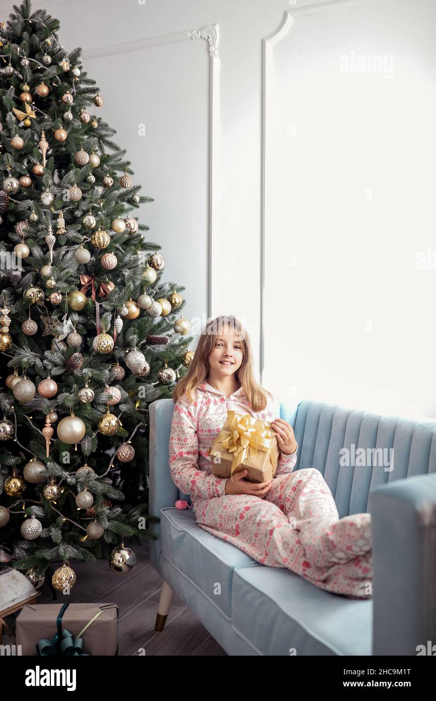 Teenager-Mädchen mit einem Geschenk in der Nähe eines Neujahrsbaums oder in einem weihnachtlichen Interieur. Stockfoto
