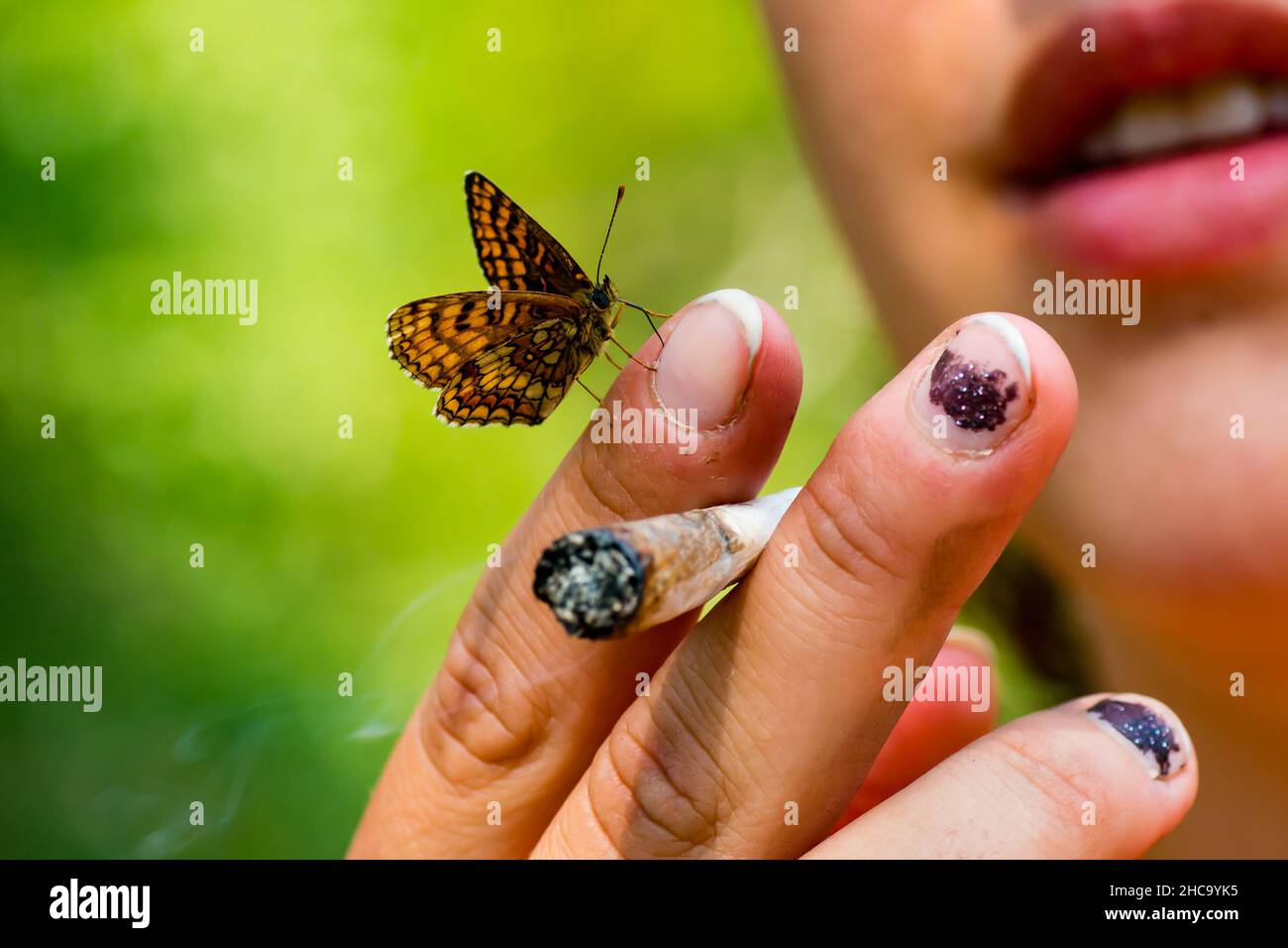 Nahaufnahme einer Hand, die eine Zigarette mit einem Schmetterling auf sich hält Stockfoto