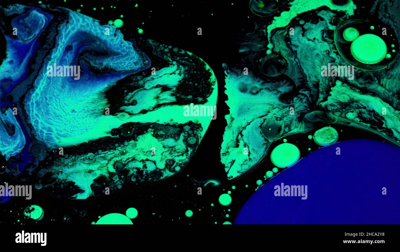 Nahaufnahme der grünen und blauen Ölfarbe, die in schwarze Tinten eingefügt wird. Mischflüssigkeit Farben Textur auf schwarzem Hintergrund, Kunst und Kreativität Konzept. Stockfoto