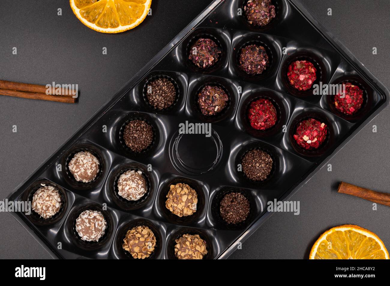 Bunte Schokoladentrüffel in einer Süßkarton mit Zimt und getrockneten Orangen auf schwarzem Hintergrund. Draufsicht. Stockfoto