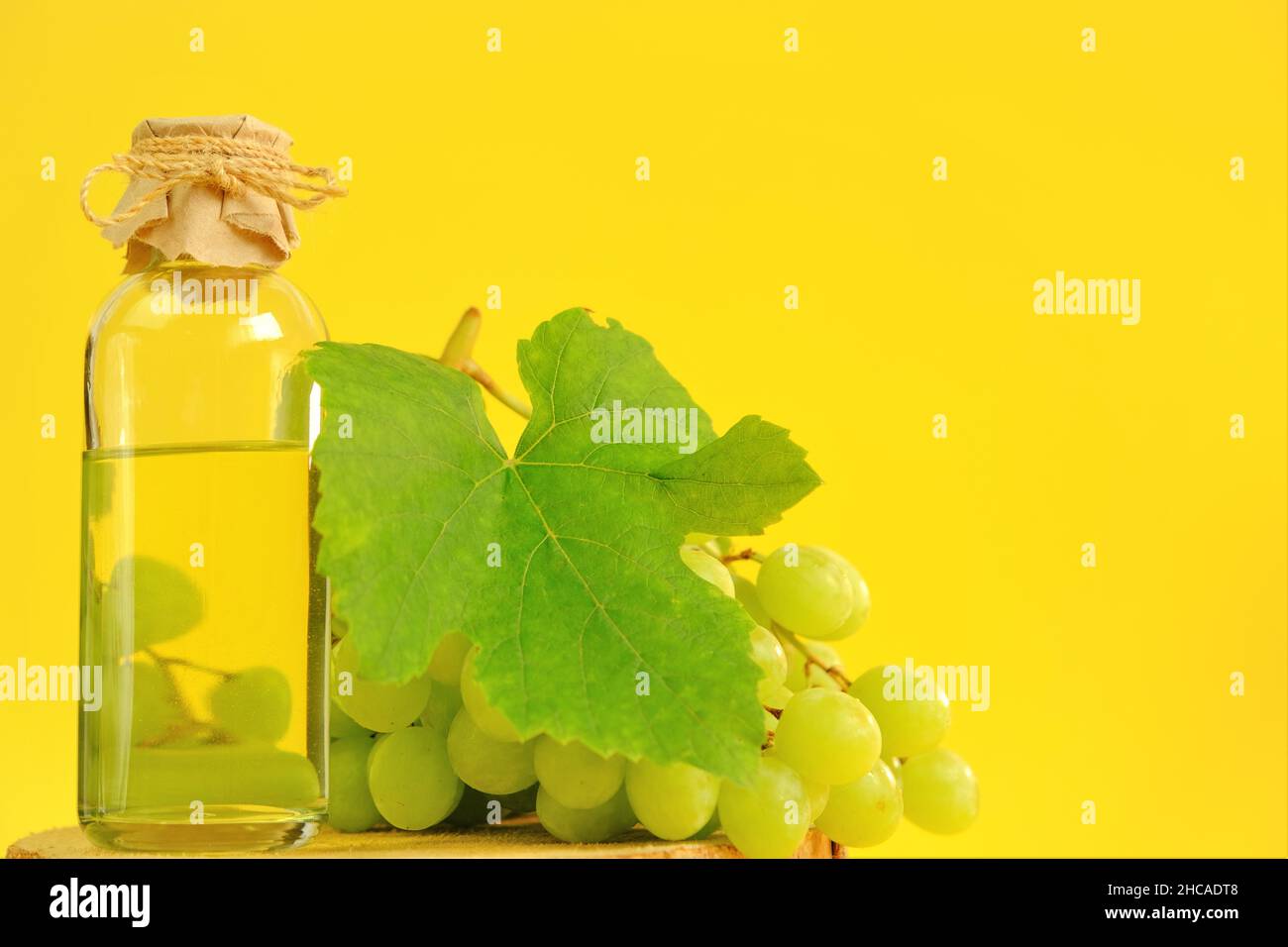 Traubenkernöl.Basis-Kosmetiköl für Massage und Pflege für Gesicht und Körper. Flasche und Bund von grünen Trauben auf einer gelben background.Organic Bio-Traube Stockfoto