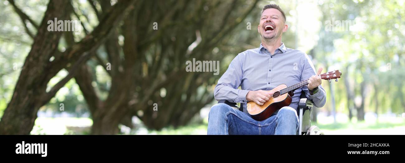 Mann im Rollstuhl spielt Gitarre im Park und verdient Geld Stockfoto
