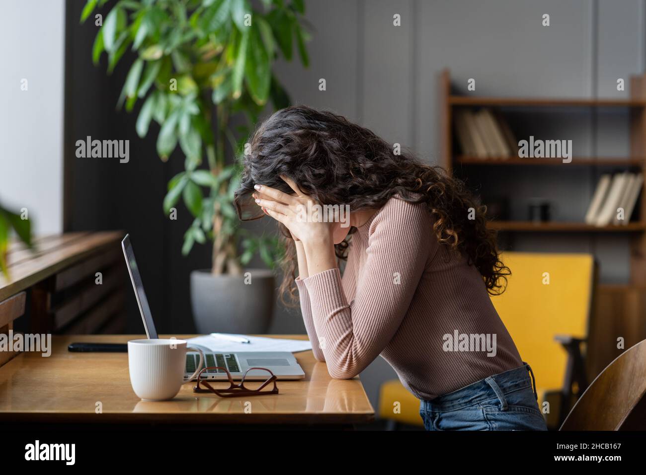 Erschöpfte unglückliche Frau sitzt am Laptop, versteckt das Gesicht in den Händen müde Überstunden leiden unter Burnout Stockfoto
