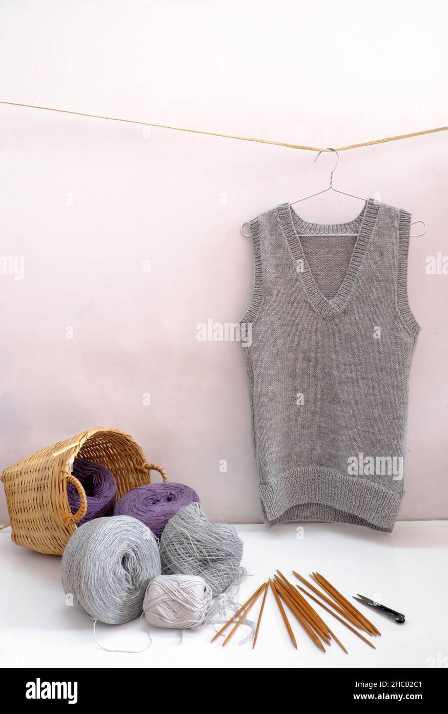 Handgemachtes Produkt, um Geschenk für die Wintersaison zu machen, Ball aus Garn Material für Strick und Mann Weste in grau hängen auf weißem Hintergrund, Handarbeit mit Wolle c Stockfoto