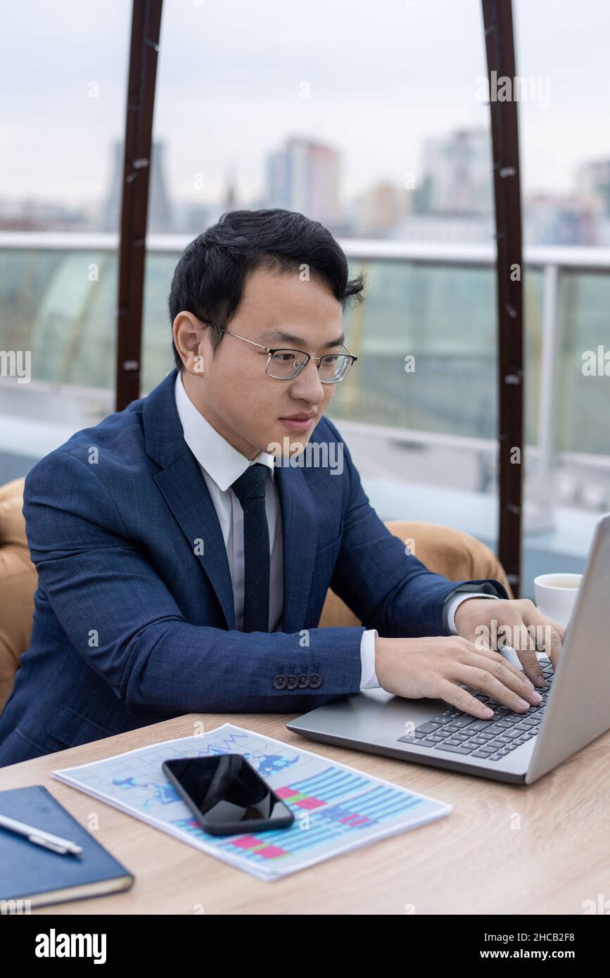 Junge chinesische Broker tippen auf dem Laptop-Tastenfeld, während sie Finanzdaten eingeben oder mit ausländischen Partnern im Netz kommunizieren Stockfoto